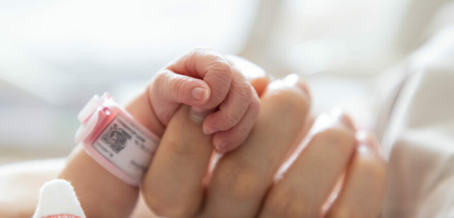 Pequeña mano de bebé recién nacido sosteniendo dedo de su mamá en una clínica porque cuenta con seguro para bebé